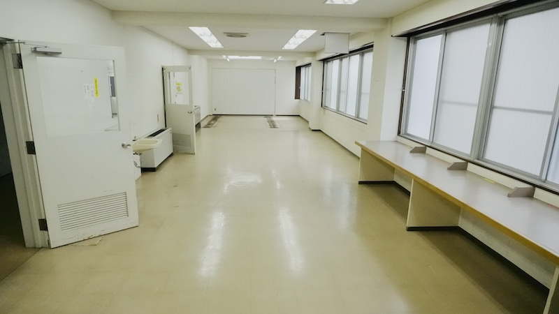 大きな窓のある明るい図書室。壁沿いに長いカウンターが設置されている