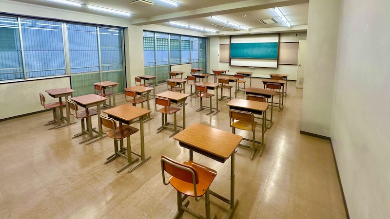 机と椅子が並んだ教室の室内写真。正面に黒板がある